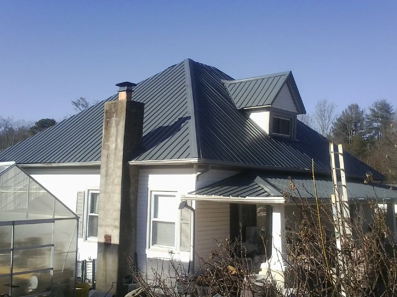Dark blue standing seam metal roof on a white farmhouse with dormer — Slate & Tile Roof Repair by Roofing Brothers in Lillian
