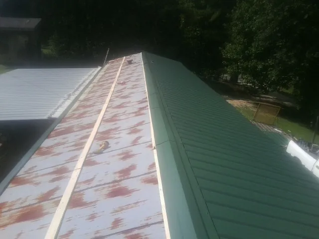 Old rusted panels beside newly installed green metal roofing — Wind Damage Roof Repair by Roofing Brothers in Lillian
