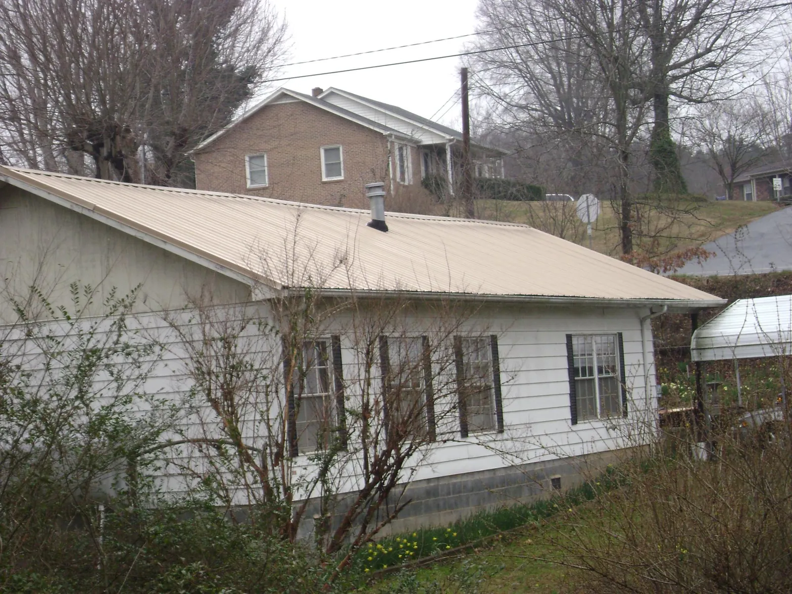 Tan metal roof on a white sided house set into a hillside — Commercial Roofing by Roofing Brothers in Lillian